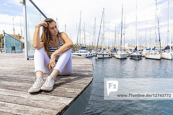 Young woman sitting on promenade at a marina