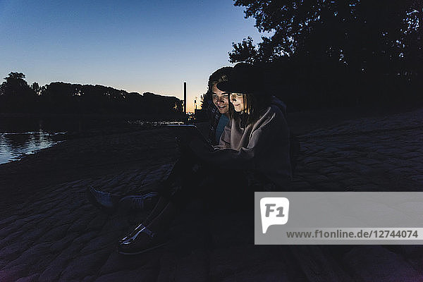 Young couple using tablet at the riverside in the evening