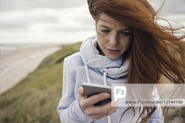Redheaded woman using smartphone on the beach