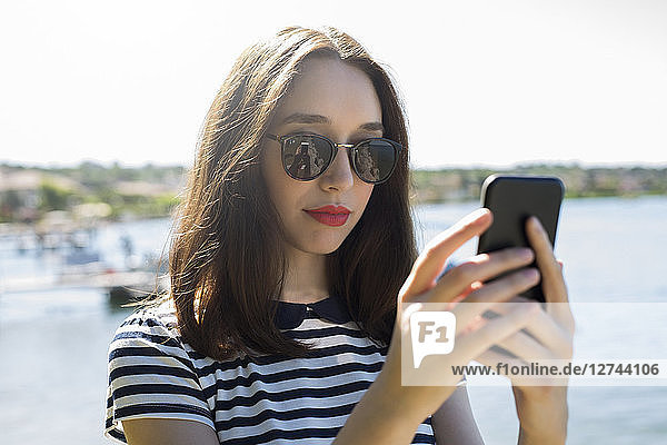 Italy  Lake Garda  portrait of young woman wearing sunglasses using smartphone