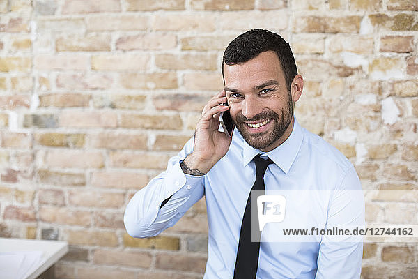 Portrait of smiling businessman on the phone at brick wall