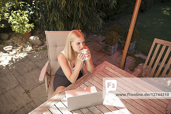 Young woman drinking coffee  laptop on garden table