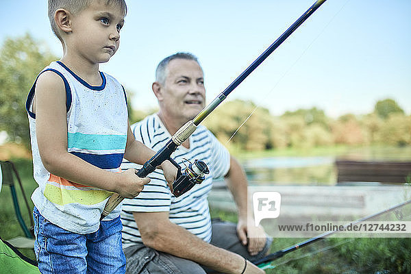 Little boy fishing together with his grandfather at lakeshore