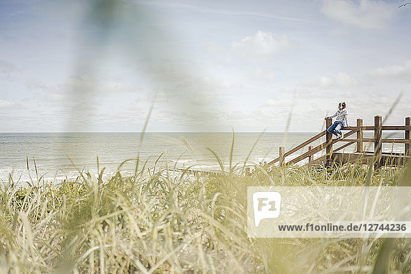 Woman sitting on fence at the sea  wearing headphones