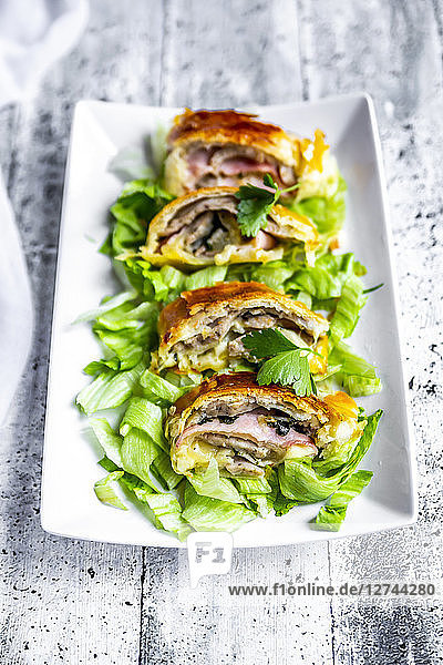 Swiss roll  puff pastry with sausage meat  cheese  onion  parsley and salad on plate