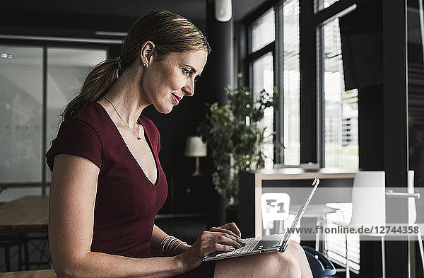 Businesswoman in office wearing burgundy dress using laptop