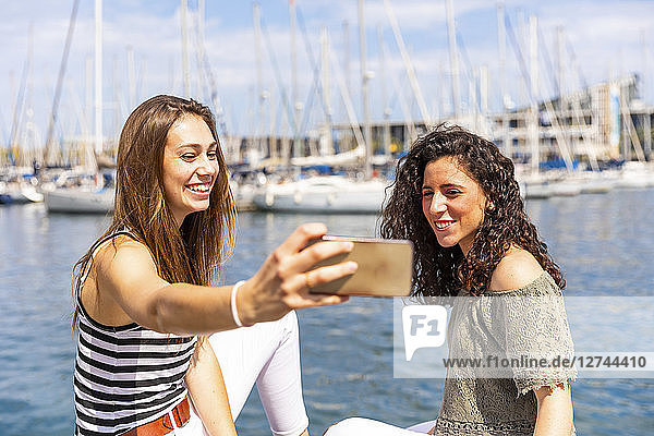 Two happy female friends taking a selfie at a marina