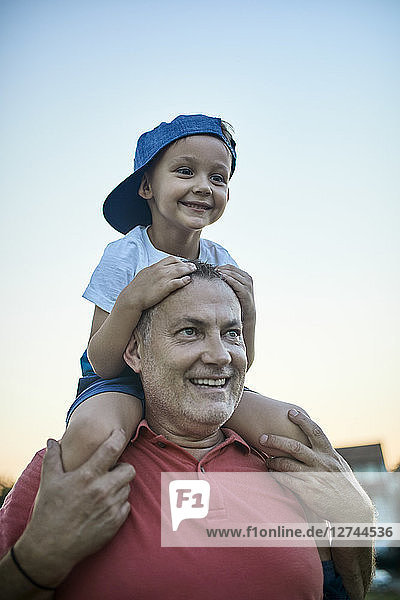 Portrait of happy little boy on shoulders of his grandfather