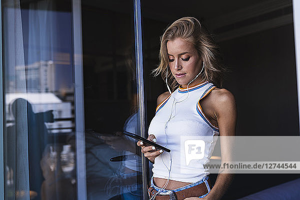 Woman in hotel room  using smartphone with earphones