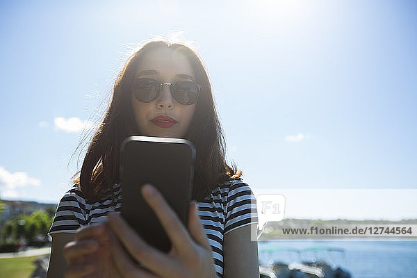 Italy  Lake Garda  portrait of young woman wearing sunglasses using smartphone
