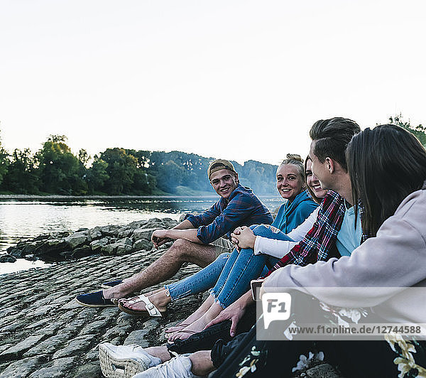 Group of friends sitting at the riverside in the evening