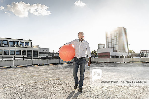 Mature man playing with orange fitness ball on rooftop of a high-rise building