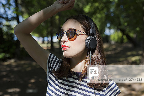 Portrait of young woman wearing sunglasses listening music with headphones