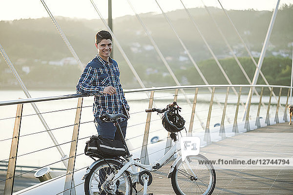 Portrait of smiling young man with folding bicycle on a bridge