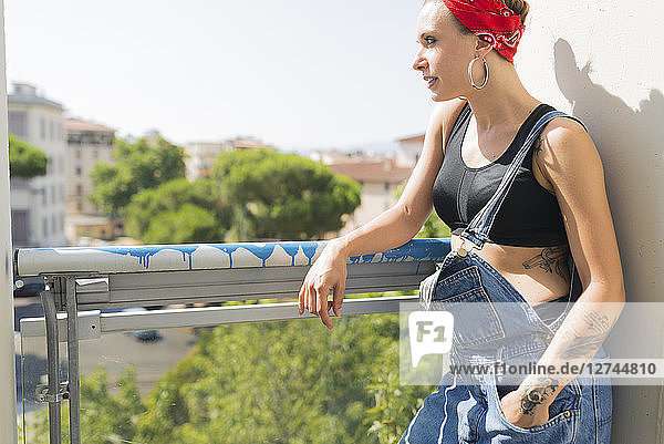 Tattooed young woman standing on balcony looking at distance