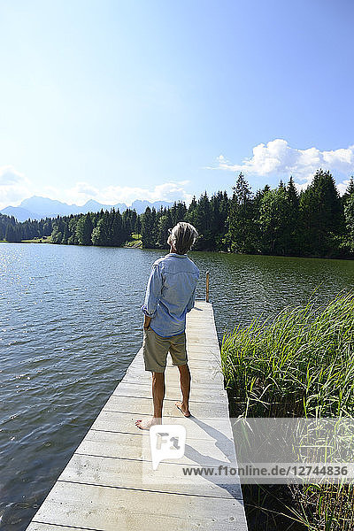 Germany  Mittenwald  back view of mature man standing barefoot on jetty at lake relaxing