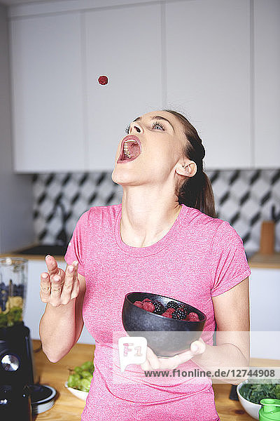 Young woman throwing raspberry in the air in the kitchen