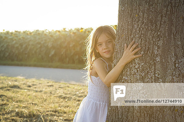 Girl leaning on tree trunk at summer evening