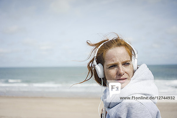 Redheaded woman relaxing at the beach  listening music with headphones