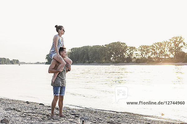 Young man carrying girlfriend on shoulders at the riverbank