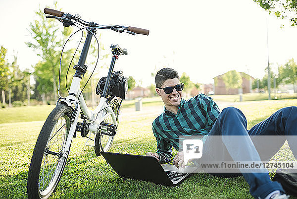 Young man with bicycle using laptop in a park