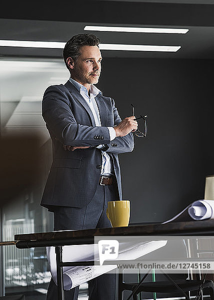 Businessman standing in office with plan on desk