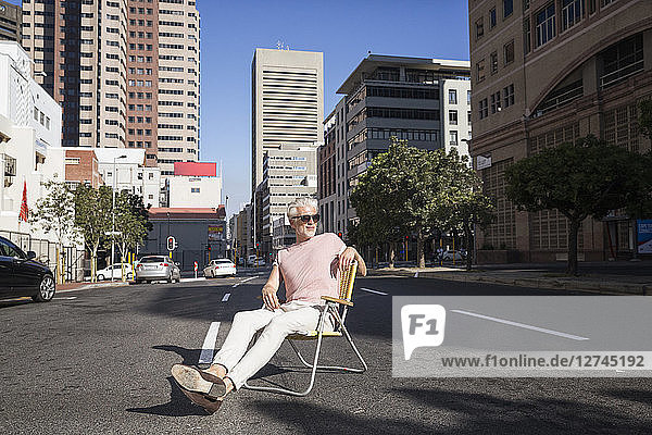 Mature man sitting on chair in the street  wearing sunglasses