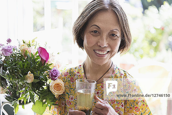 Portrait smiling  confident senior woman drinking tea next to flower bouquet