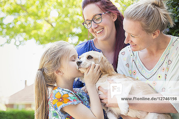 Affectionate lesbian couple and daughter kissing dog