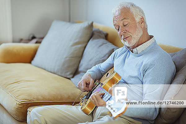 Active senior man playing guitar on living room sofa
