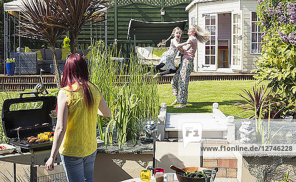 Lesbian couple and daughter playing and barbecuing in sunny backyard