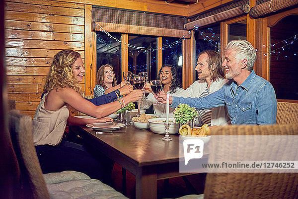 Friends toasting red wine glasses  enjoying dinner at cabin dining room table