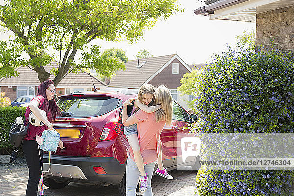 Affectionate lesbian couple and daughter at car in sunny driveway