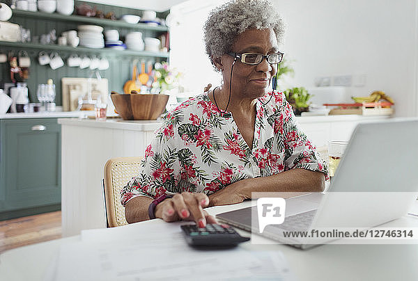 Senior woman paying bills at laptop in kitchen