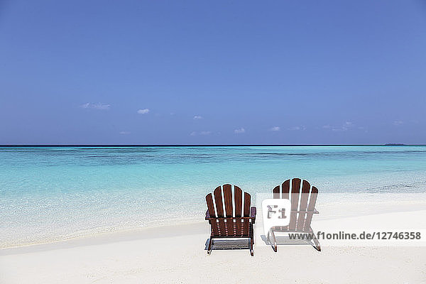Zwei Adirondack-Stühle am sonnigen  ruhigen Strand mit Blick auf den blauen Ozean  Malediven  Indischer Ozean