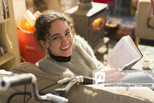 Porträt einer lächelnden  glücklichen jungen Frau  die im Sessel ein Buch liest