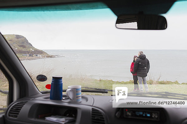 Ehepaar unterhält sich vor einem Wohnmobil auf einer Klippe mit Blick auf das Meer