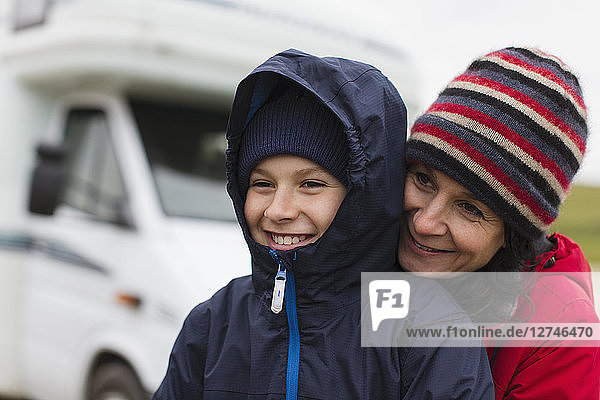 Zärtliche Mutter und Sohn in warmer Kleidung umarmen sich vor dem Wohnmobil