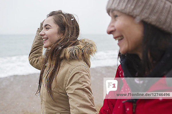 Happy mother and daughter walking on snowy beach