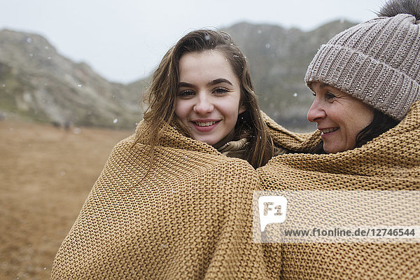 Portrait sorglose Mutter und Tochter in eine Decke eingewickelt am verschneiten Winterstrand