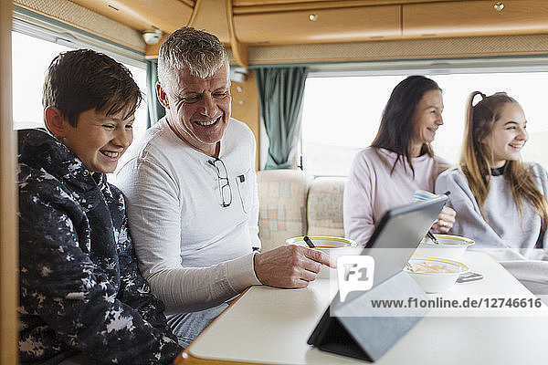 Family relaxing  eating breakfast and using digital tablet in motor home