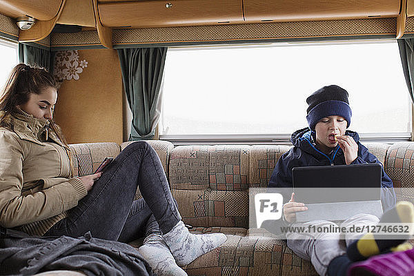 Bruder und Schwester im Teenageralter benutzen Tablet und Smartphone im Wohnmobil