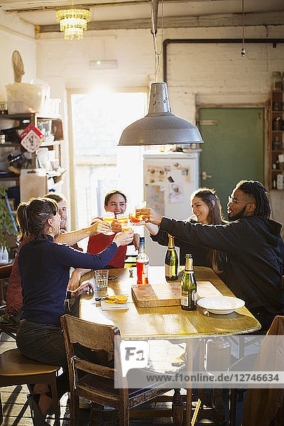 Young adult friends toasting cocktails at apartment kitchen table