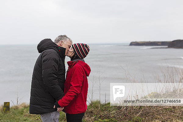 Affectionate couple kissing on cliff overlooking ocean