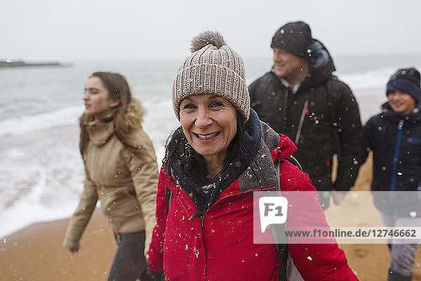 Portrait smiling woman in warm clothing with family on snowy winter ocean beach