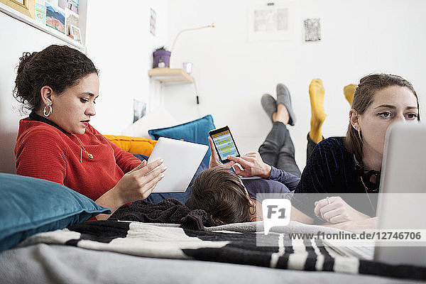Young women friends hanging out  using smart phone  digital tablet and laptop on bed
