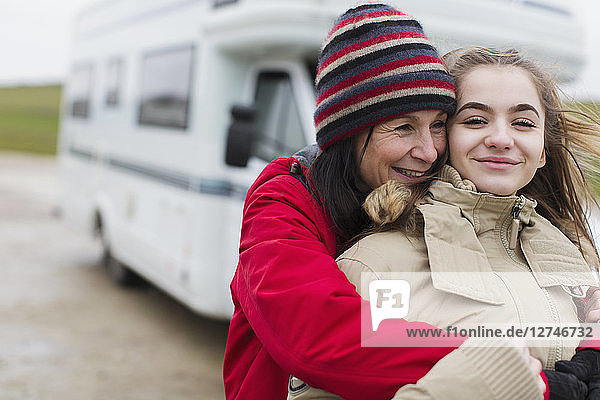 Zärtliche Mutter und Tochter in warmer Kleidung umarmen sich vor dem Wohnmobil