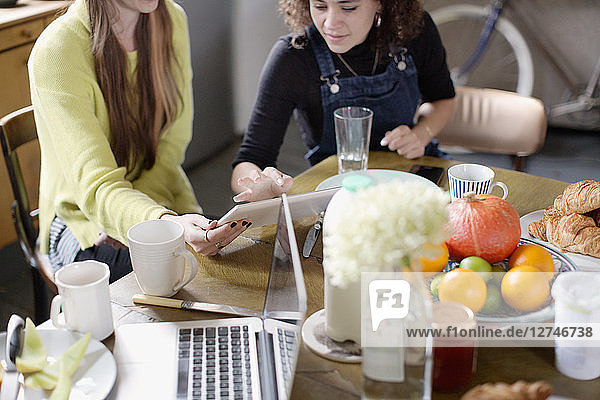 Junge Frauen  die mit Freunden zusammenwohnen und am Frühstückstisch ein digitales Tablet benutzen