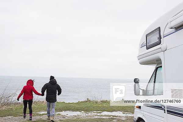 Paar hält sich vor einem Wohnmobil mit Blick auf das Meer an den Händen