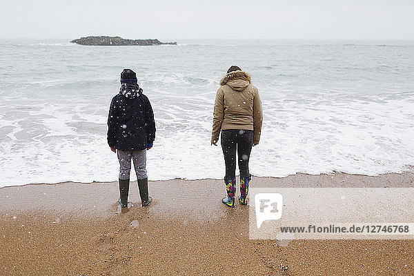 Brother and sister in warm clothing standing on snowy winter beach